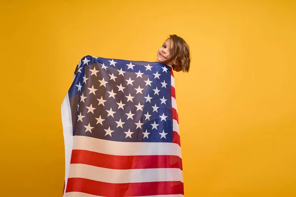 Šťastné dítě, roztomilá dívka s americkou vlajkou na žlutém pozadí studia. USA slaví 4. července, Den nezávislosti. — Stock fotografie