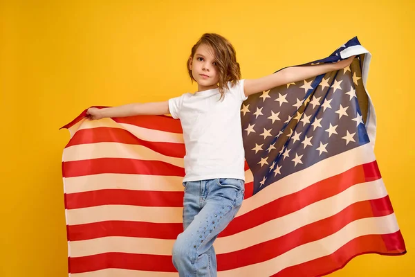 Šťastné dítě, roztomilá dívka s americkou vlajkou na žlutém pozadí studia. USA slaví 4. července, Den nezávislosti. — Stock fotografie