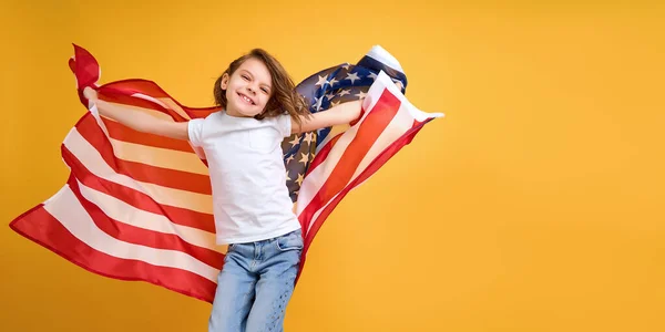 Šťastné dítě, roztomilá dívka s americkou vlajkou na žlutém pozadí studia. USA slaví 4. července, Den nezávislosti. — Stock fotografie