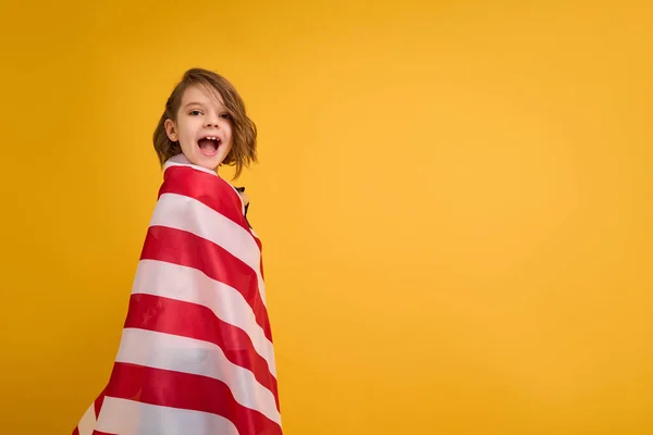 Šťastné dítě, roztomilá dívka s americkou vlajkou na žlutém pozadí studia. USA slaví 4. července, Den nezávislosti. — Stock fotografie