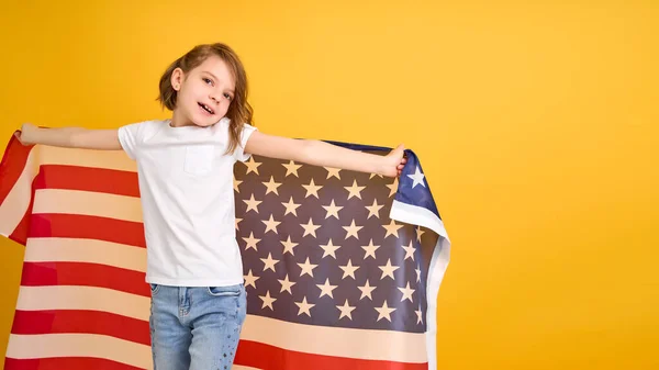 Happy child, cute girl with American flag on yellow studio background. USA celebrate July 4th, independence Day. Stock Photo