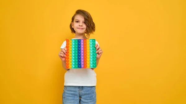 Little girl holding pop it antistress toy on yellow background — Stock Photo, Image