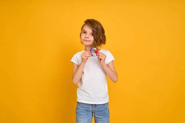Little girl holding pop it antistress toy on yellow background — Stock Photo, Image