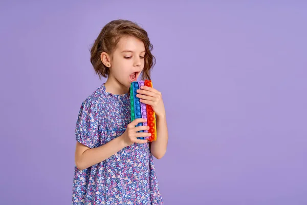 Teen age Girl in blue summer flower print dress holding pop it antistress toy on lavender background, isolate. — Stock Photo, Image