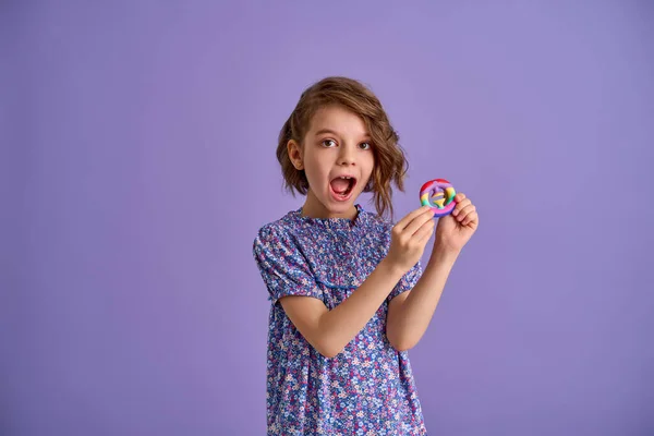 Teen age Girl in blue summer flower print dress holding pop it antistress toy on lavender background, isolate. — Stock Photo, Image