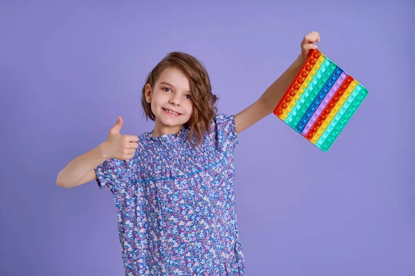 Teen age Girl in blue summer flower print dress holding pop it antistress toy on lavender background, isolate. — Stock Photo, Image