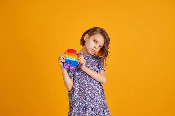 Little girl holding pop it antistress toy on yellow background — Stock Photo, Image