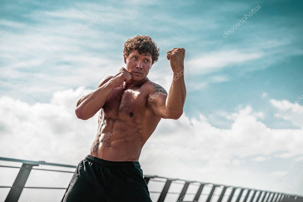 Muscular young man athlete standing and practicing shadow boxing outdoors early in the morning on pier by the sea