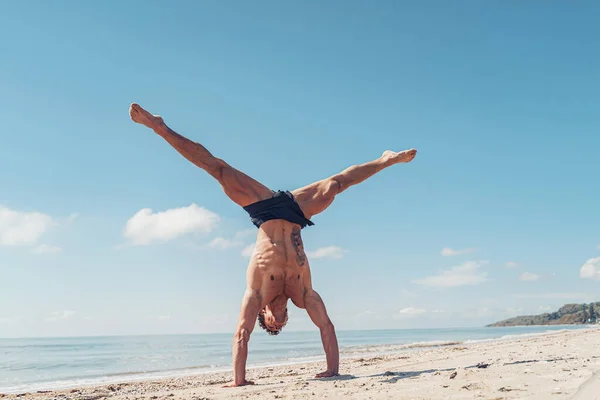 Svalnatý kulturista fitness muž s nahým trupem stojí na paži na pláži — Stock fotografie