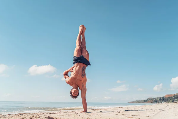 Svalnatý kulturista fitness muž s nahým trupem stojí na jedné paži na pláži — Stock fotografie