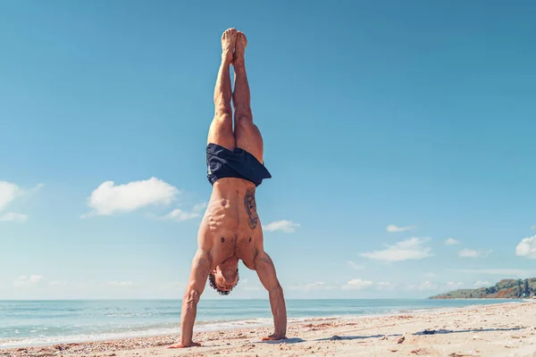 Svalnatý kulturista fitness muž s nahým trupem stojí na paži na pláži — Stock fotografie