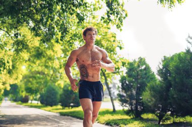 Parkta üstsüz koşan güçlü ve çekici bir adam.