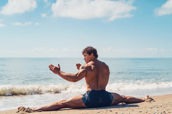 Homme athlétique avec de beaux muscles est assis sur une ficelle dans l'entraînement d'été au bord de la mer — Photo