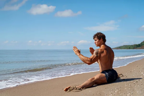 Atletický muž s krásnými svaly sedí na provázku v letním tréninku na pobřeží — Stock fotografie