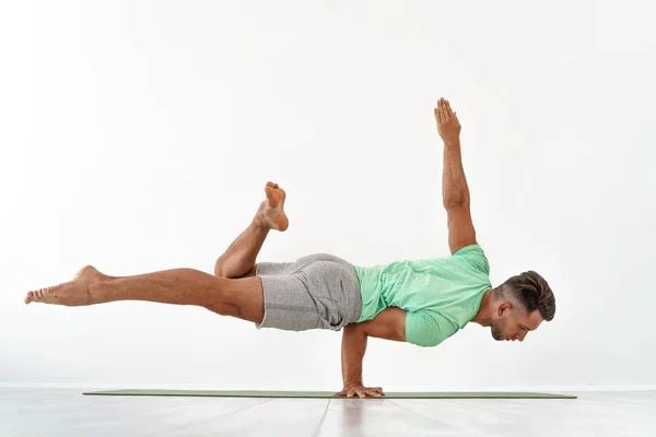 Homem praticando equilíbrio ioga pose no fundo do estúdio branco — Fotografia de Stock