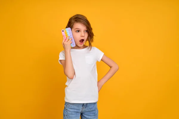 Surprized little girl holding telephone with open mouth isolated over yellow color background — Stock Photo, Image