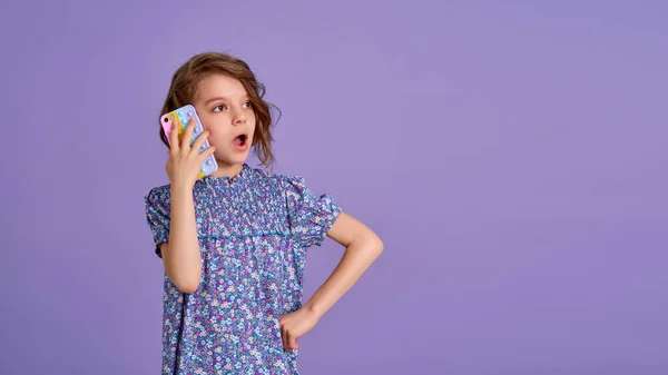 Surprized little girl holding telephone with open mouth isolated over violet color background — Stock Photo, Image