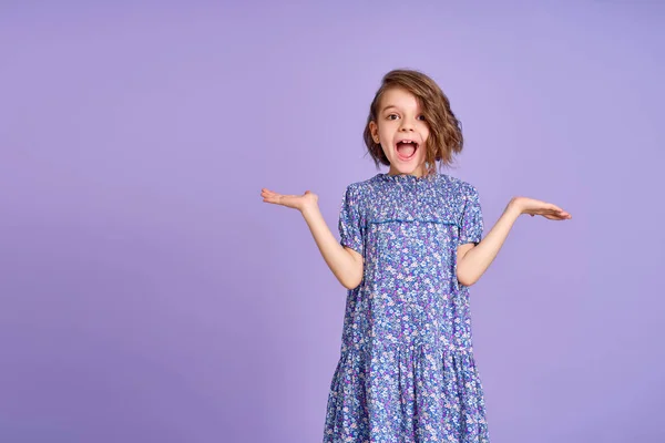 Photo of young happy surprised girl spread her hands to the sides isolated on purple color background — Stock Photo, Image