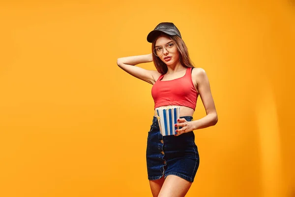 Mujer alegre de pie con palomitas de maíz sobre fondo amarillo. — Foto de Stock