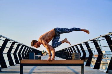 Şafak vakti okyanus kıyısında gökyüzüne karşı yoga yaparken el standı yapan zinde bir adam.