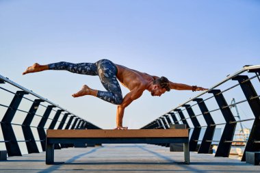 Şafak vakti okyanus kıyısında gökyüzüne karşı yoga yaparken el standı yapan zinde bir adam.