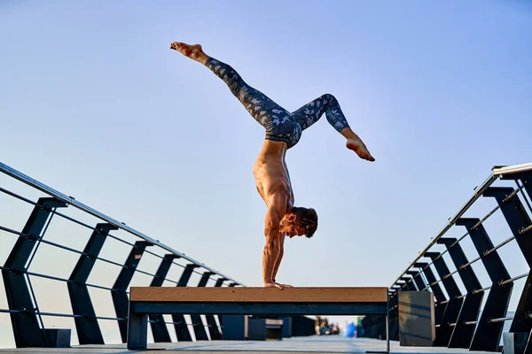 Ajustez l'homme faisant un stand de main tout en pratiquant le yoga seul près de l'océan contre le ciel au crépuscule ou à l'aube — Photo