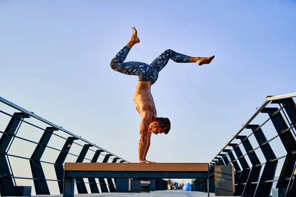 Ajustez l'homme faisant un stand de main tout en pratiquant le yoga seul près de l'océan contre le ciel au crépuscule ou à l'aube — Photo