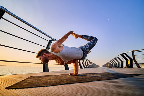 Ajuste al hombre haciendo una parada de una mano mientras practica yoga solo cerca del océano contra el cielo al atardecer o al amanecer —  Fotos de Stock