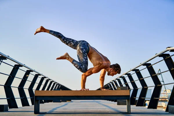 Ajustez l'homme faisant un stand de main tout en pratiquant le yoga seul près de l'océan contre le ciel au crépuscule ou à l'aube — Photo