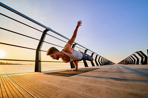 Ajustez l'homme faisant un stand d'une main tout en pratiquant le yoga seul près de l'océan contre le ciel au crépuscule ou à l'aube — Photo