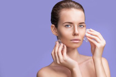 Yüzünün yanında buz küpleri tutan doğal makyajlı güzel bir kadın.