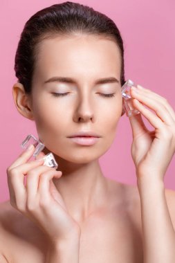 Yüzünün yanında buz küpleri tutan doğal makyajlı güzel bir kadın.