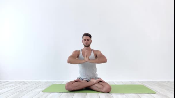 Yoga masculino medita en pose clásica en estudio sobre fondo blanco — Vídeo de stock