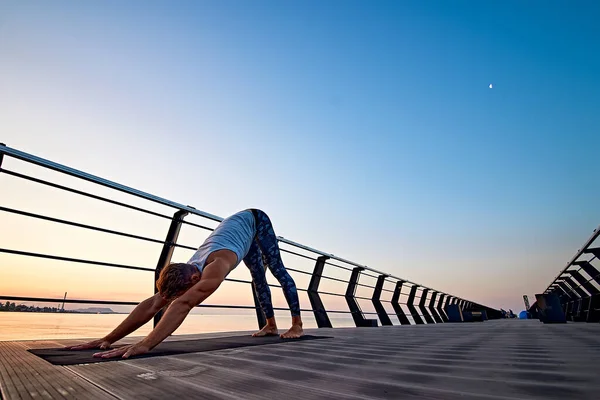 Muž cvičí jógu při západu slunce a dělá psí ksicht dolů — Stock fotografie