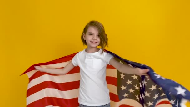 Patriotisk högtid. Glad barn, söt flicka med amerikansk flagga på gul studio bakgrund. USA firar 4 juli, självständighetsdagen — Stockvideo