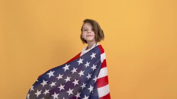 Patriotisk högtid. Glad barn, söt flicka med amerikansk flagga på gul studio bakgrund. USA firar 4 juli, självständighetsdagen — Stockvideo