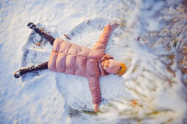 Küçük tatlı kız dışarıda kar meleği yapıyor. Çocuklar açık hava aktiviteleri. Kış tatili ve tatiller
