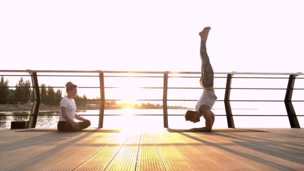 Para ćwiczących akrobatyczną jogę razem na łonie natury na morzu. Poranne ćwiczenia o wschodzie słońca — Wideo stockowe
