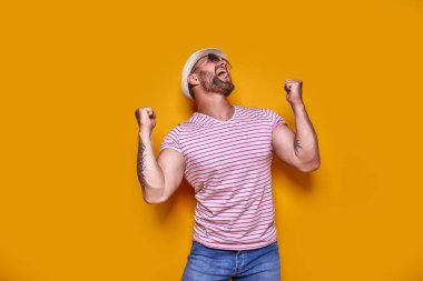 Heyecanlı, sakallı, güneş gözlüklü ve şapkalı bir adamın resmi..