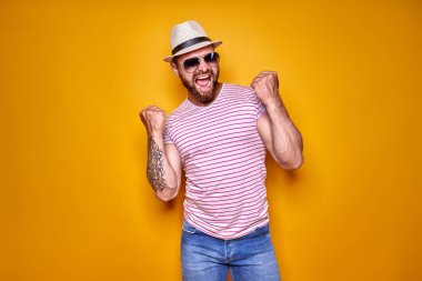 Heyecanlı, sakallı, güneş gözlüklü ve şapkalı bir adamın resmi..