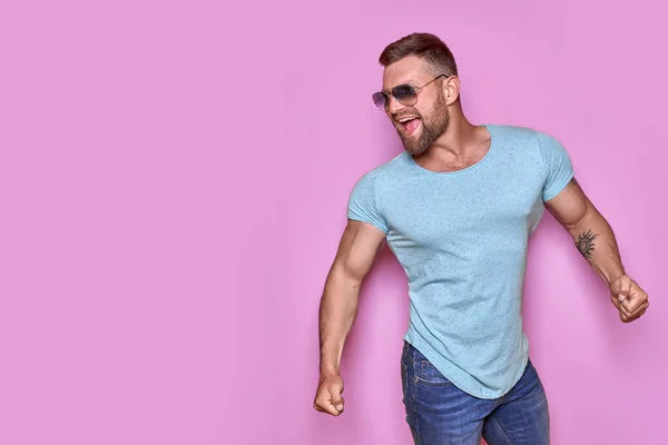 Imagen del hombre tatuado barbudo excitado en gafas de sol gesto ganador aislado fondo rosa. — Foto de Stock