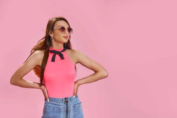 Wanita muda yang cantik memakai kacamata hitam dan topi jerami di latar belakang merah muda — Stok Foto
