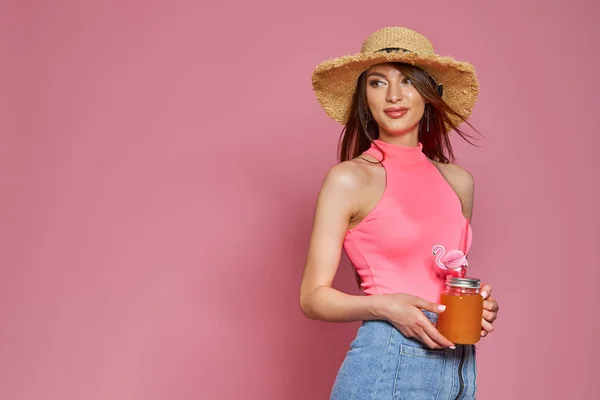 Студійний портрет красивої чарівної прекрасної леді, що тримає склянку соку в руці в солом'яному капелюсі ізольовано на рожевому фоні — стокове фото