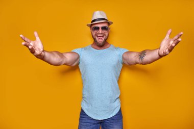 Yaklaş, sana sarılayım. Moda kıyafetli, şapkalı, arkadaş canlısı bir adamın fotoğraf stüdyosu fotoğrafı. Kameraya doğru el ele tutuşuyor. Arkadaşları içeri davet ediyor.