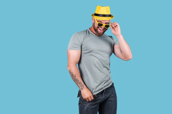 Fashionable gespierde bebaarde emotionele man in geel stro hoed poseren in studio over blauwe achtergrond — Stockfoto