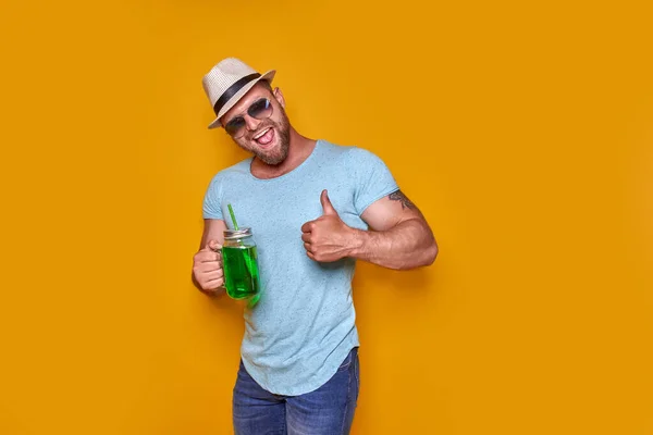 Hombre creativo en gafas de sol y ropa de verano, sombrero elegante de pie relajado y beber de la botella de cóctel creativo — Foto de Stock