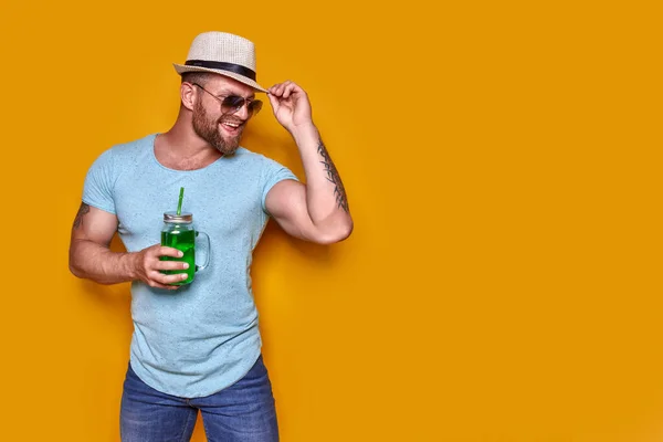 Kreativer Mann in Sonnenbrille und Sommerkleidung, stylischer Hut, entspannt stehend und aus kreativer Cocktailflasche trinkend — Stockfoto
