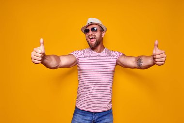 Şapkalı ve güneş gözlüklü sakallı adam baş parmağını kaldırıyor.