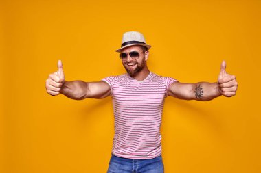Şapkalı ve güneş gözlüklü sakallı adam baş parmağını kaldırıyor.