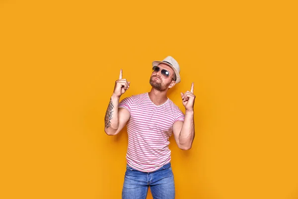 Hombre barbudo con sombrero y gafas de sol apuntando con el dedo hacia arriba — Foto de Stock